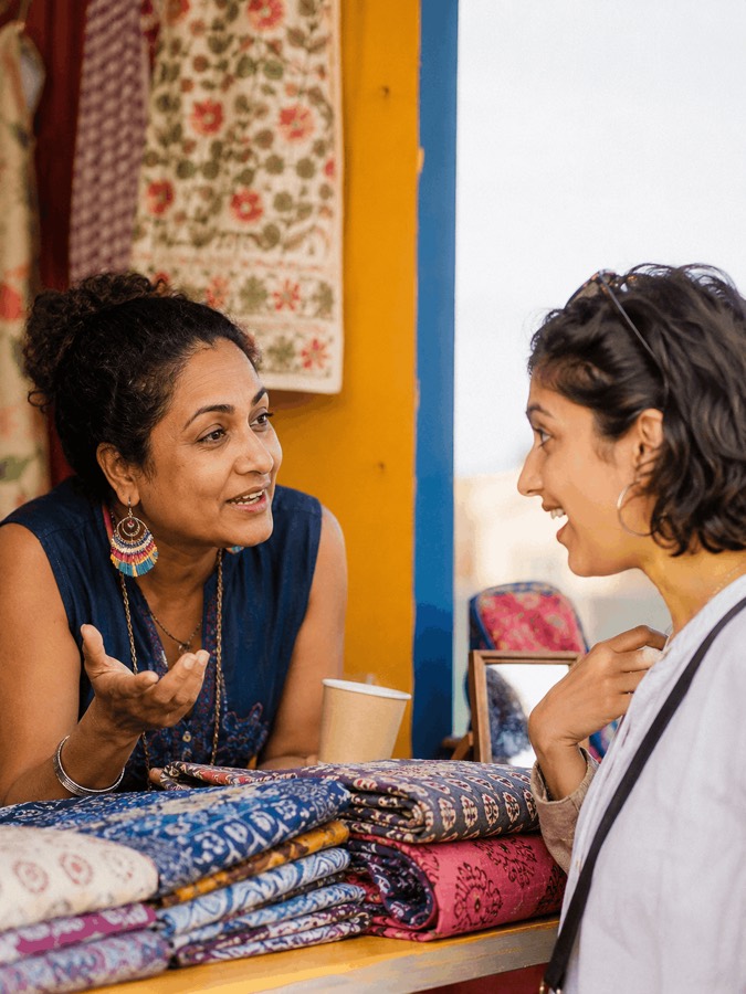 Two attendees talking over folded textiles at a bazaar stall